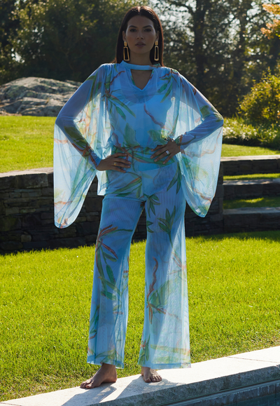 Woman wearing mesh bamboo printed blue pants with matcing mesh blue bamboo printed poncho by Ala von Auersperg for Resort 2024 by a pool