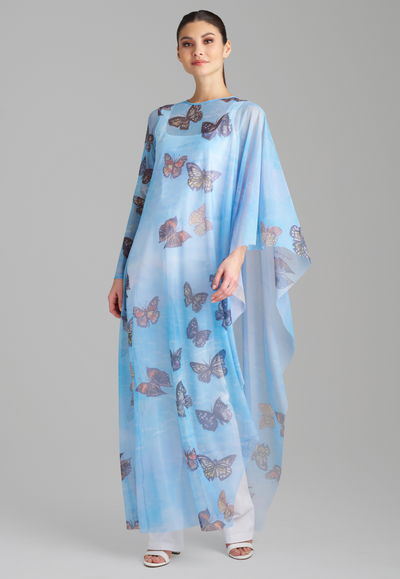 Woman wearing one armed mesh poncho kaftan in blue butterfly printed over white italian stretch cotton tank top and pants by Ala von Auersperg for spring 2023
