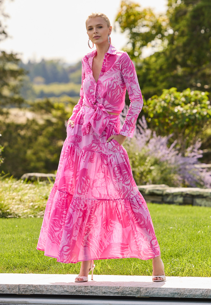 Woman wearing a pink top and skirt with a nautical pink pattern standing outdoors in a garden.