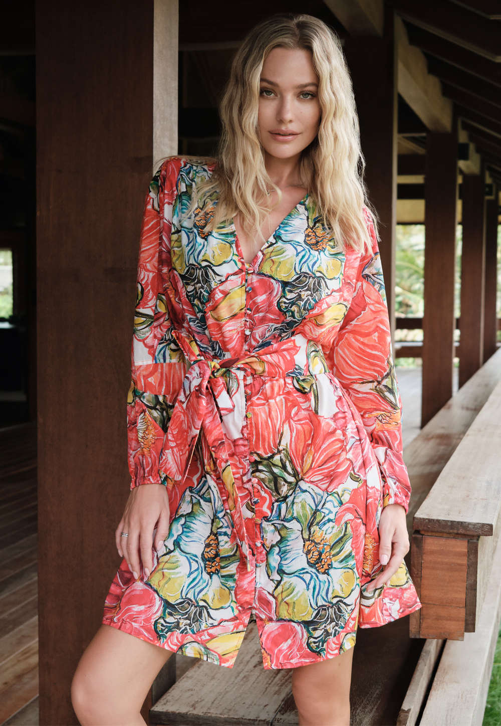 Woman wearing a colorful floral dress standing on a wooden deck.