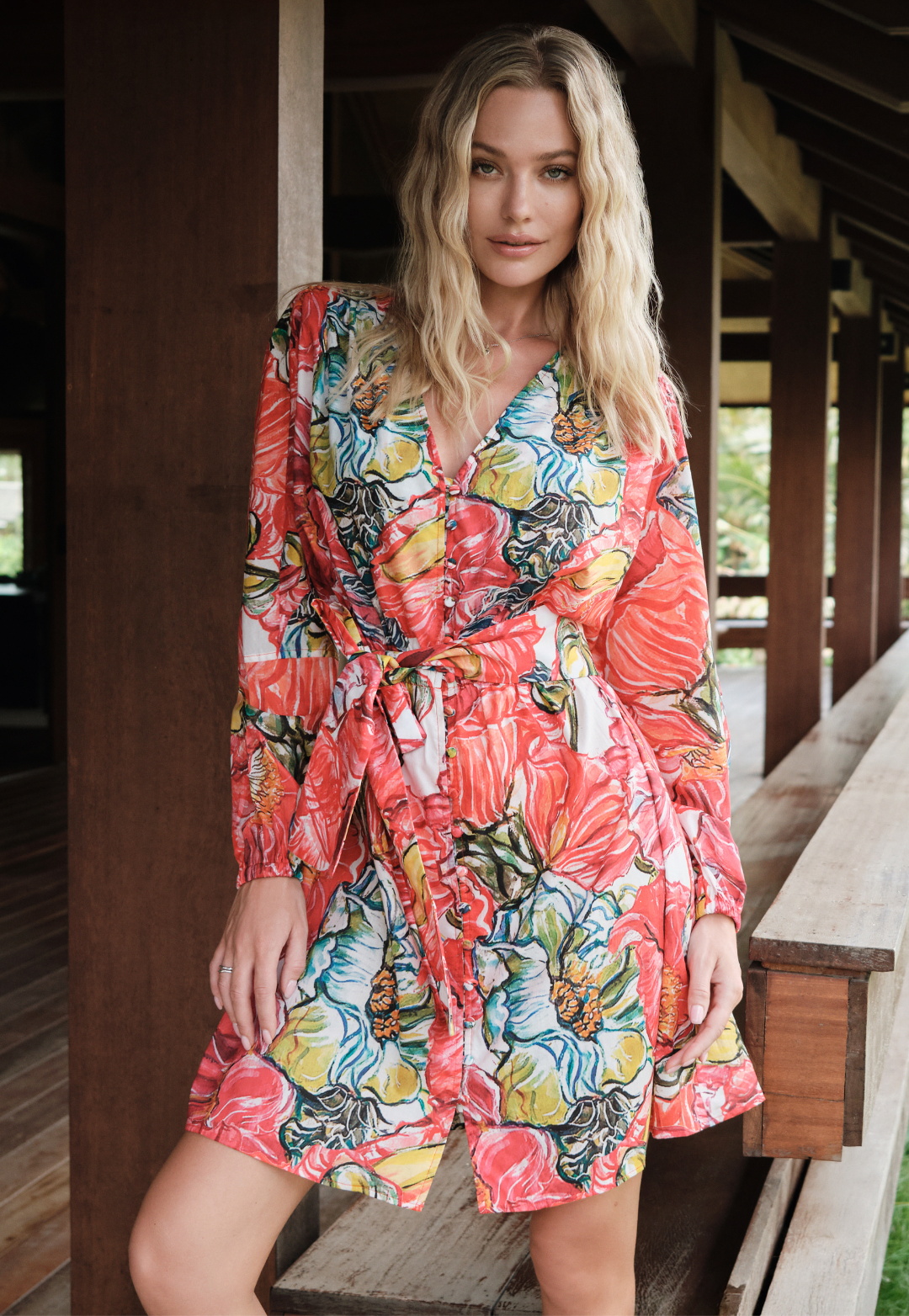 Woman wearing a colorful floral dress standing on a wooden deck.