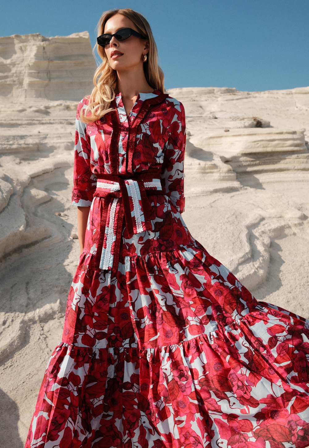 Woman in a red floral dress standing on a stone staircase with a clear blue sky.