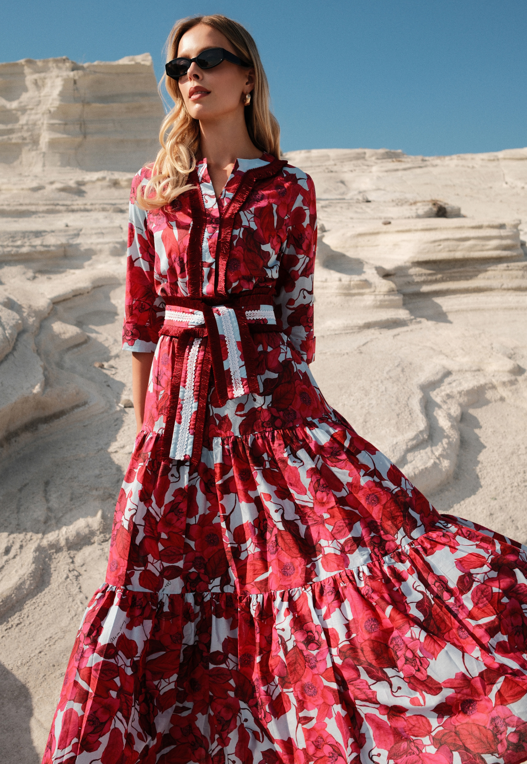 Woman in a red floral dress standing on a stone staircase with a clear blue sky.