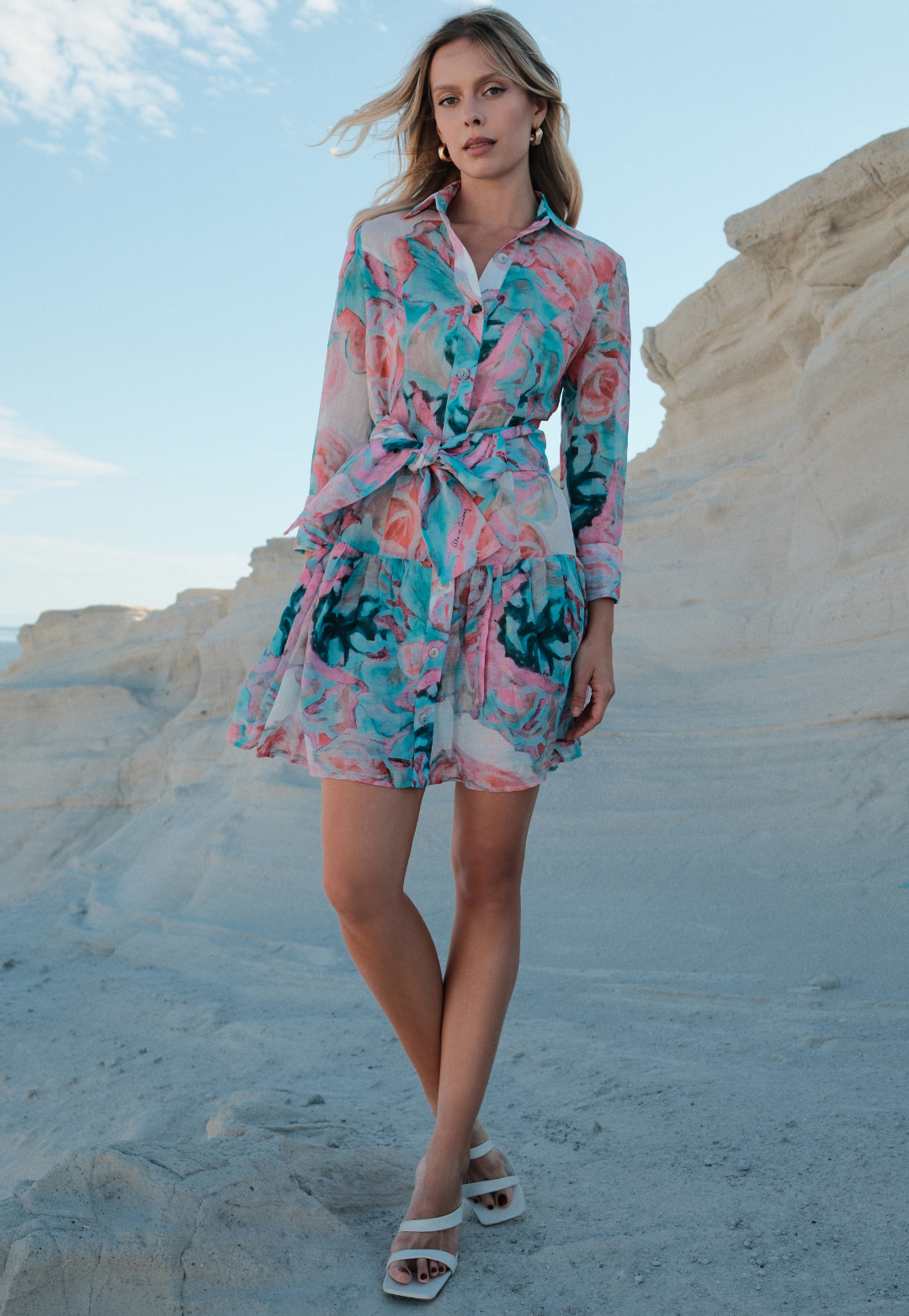 Woman wearing a floral dress standing on a sandy landscape with blue sky.