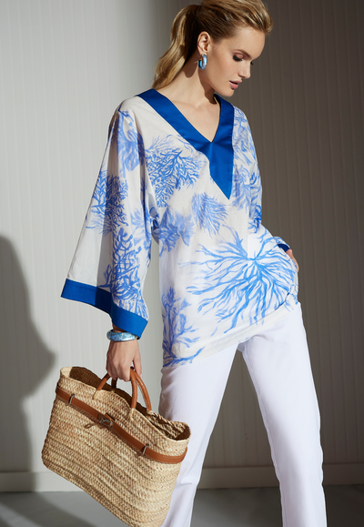 Woman wearing blue and white printed cotton tunic with blue silk trim paired with white Italian stretch cotton pants and bag by designer Ala von Auersperg for women's luxury clothing