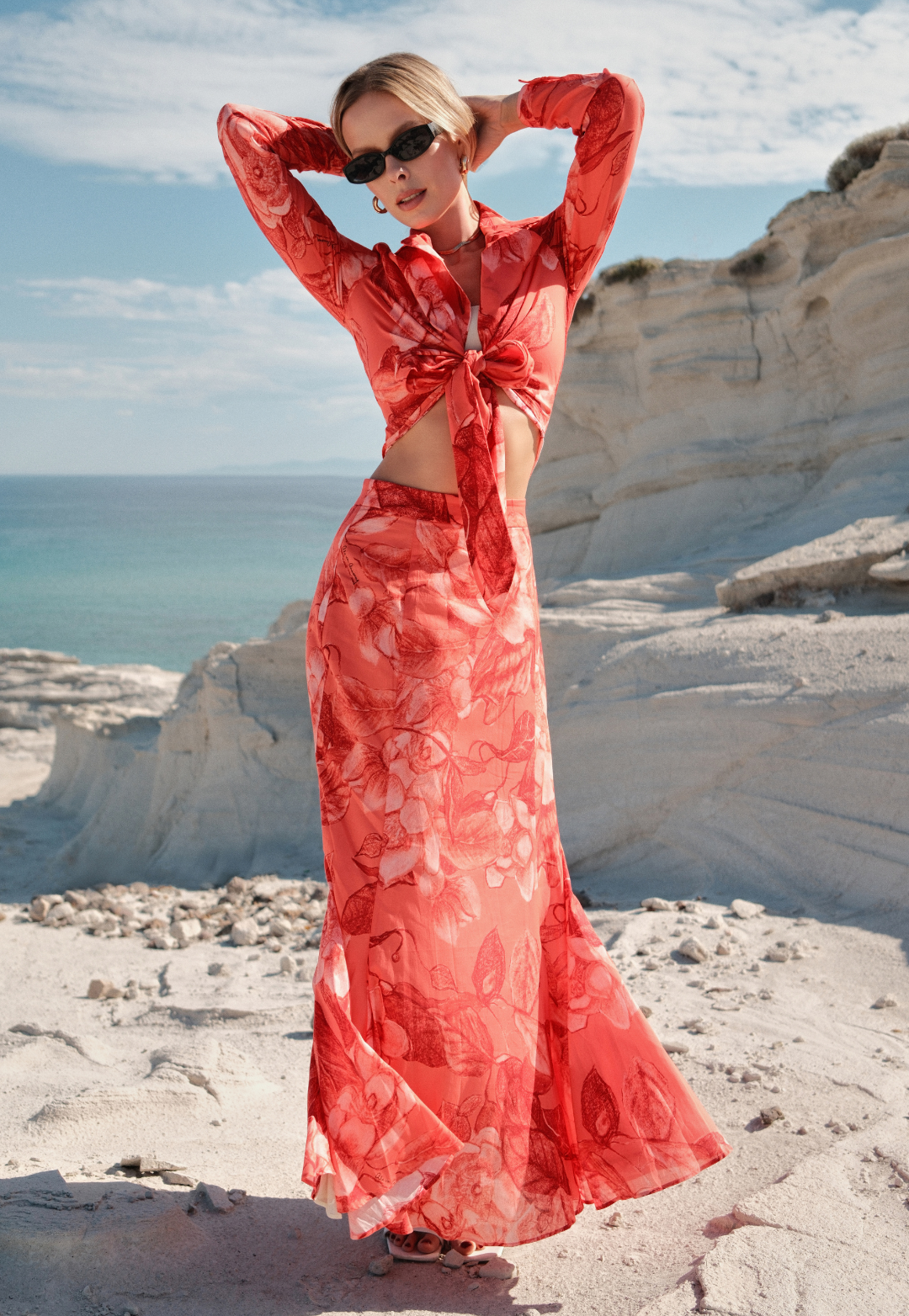 Woman in a red dress standing on a rocky beach with ocean and sky in the background