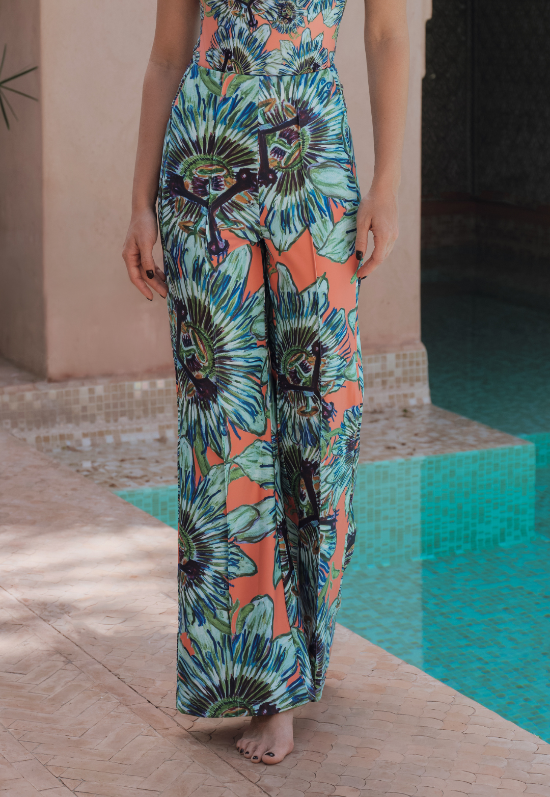 Person wearing a colorful floral pants by a poolside.