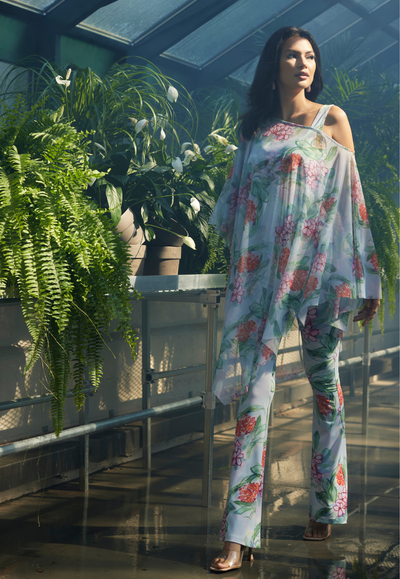 Woman in a green house wearing printed floral mesh poncho over stretch knit tank top and pants in a matching pant by Ala von Auersperg for summer 2024
