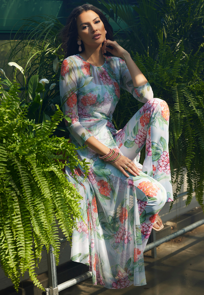 Woman wearing floral mesh dress topper over stretch knit tank top and pant in the matching print in a greenhouse for summer 2024 by Ala von Auersperg