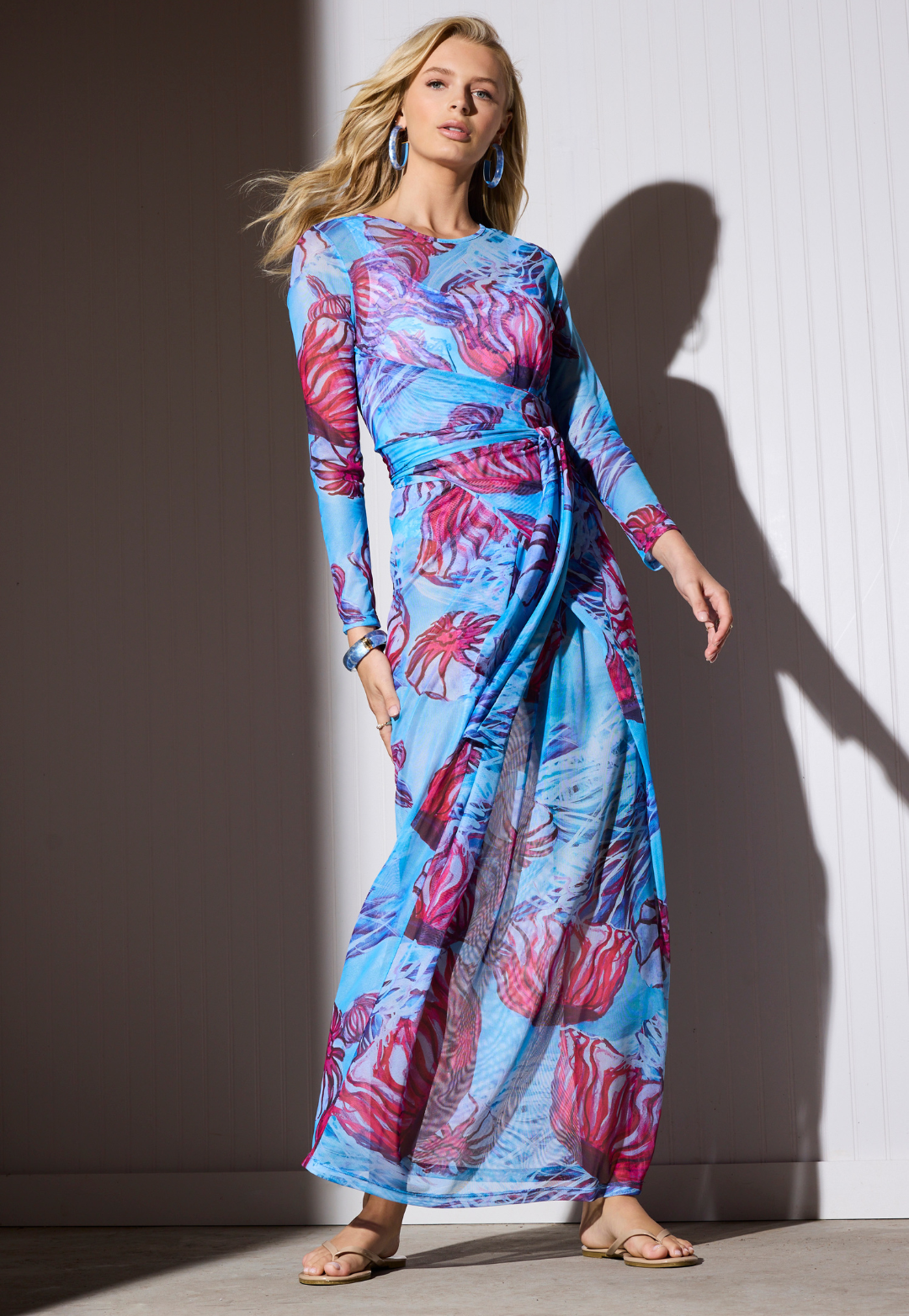 Woman wearing a colorful nautical mesh dress against a white wall.