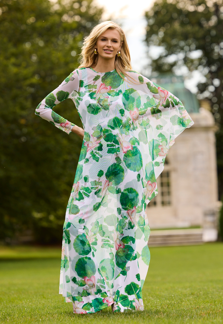 Woman wearing a floral mesh poncho standing outdoors with greenery in the background