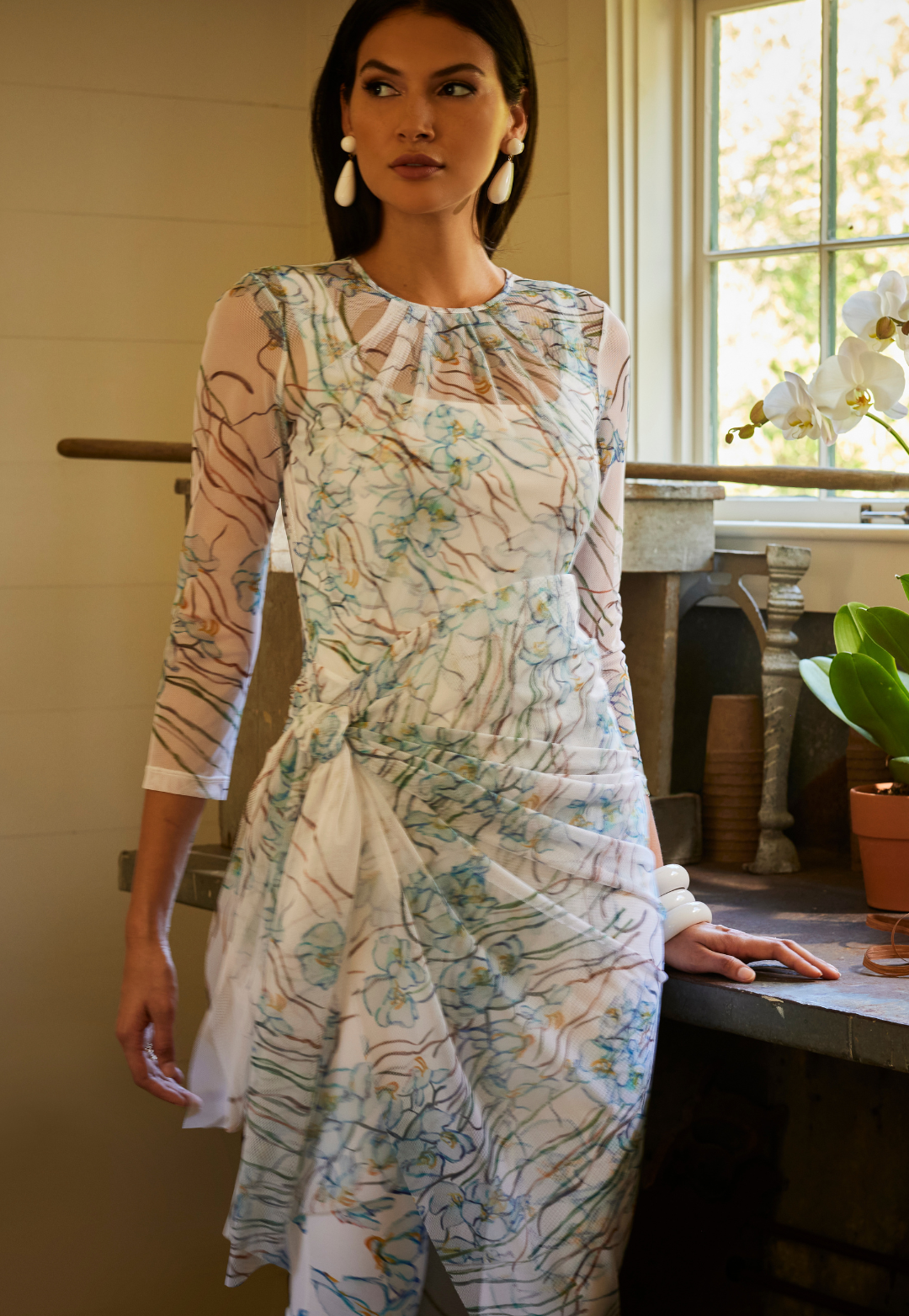 Woman wearing three piece outfit set by Ala von Auersperg with a white tank top and matching pants with a mesh orchid printed topper for spring 2024