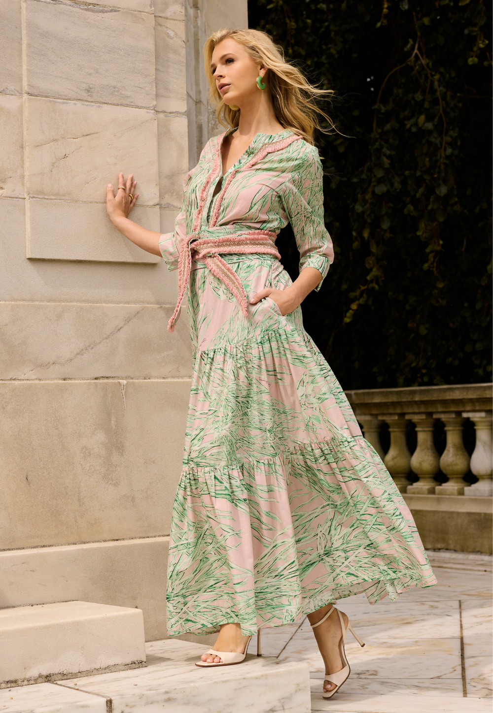 Woman in a green and pink patterned dress standing against a stone wall.