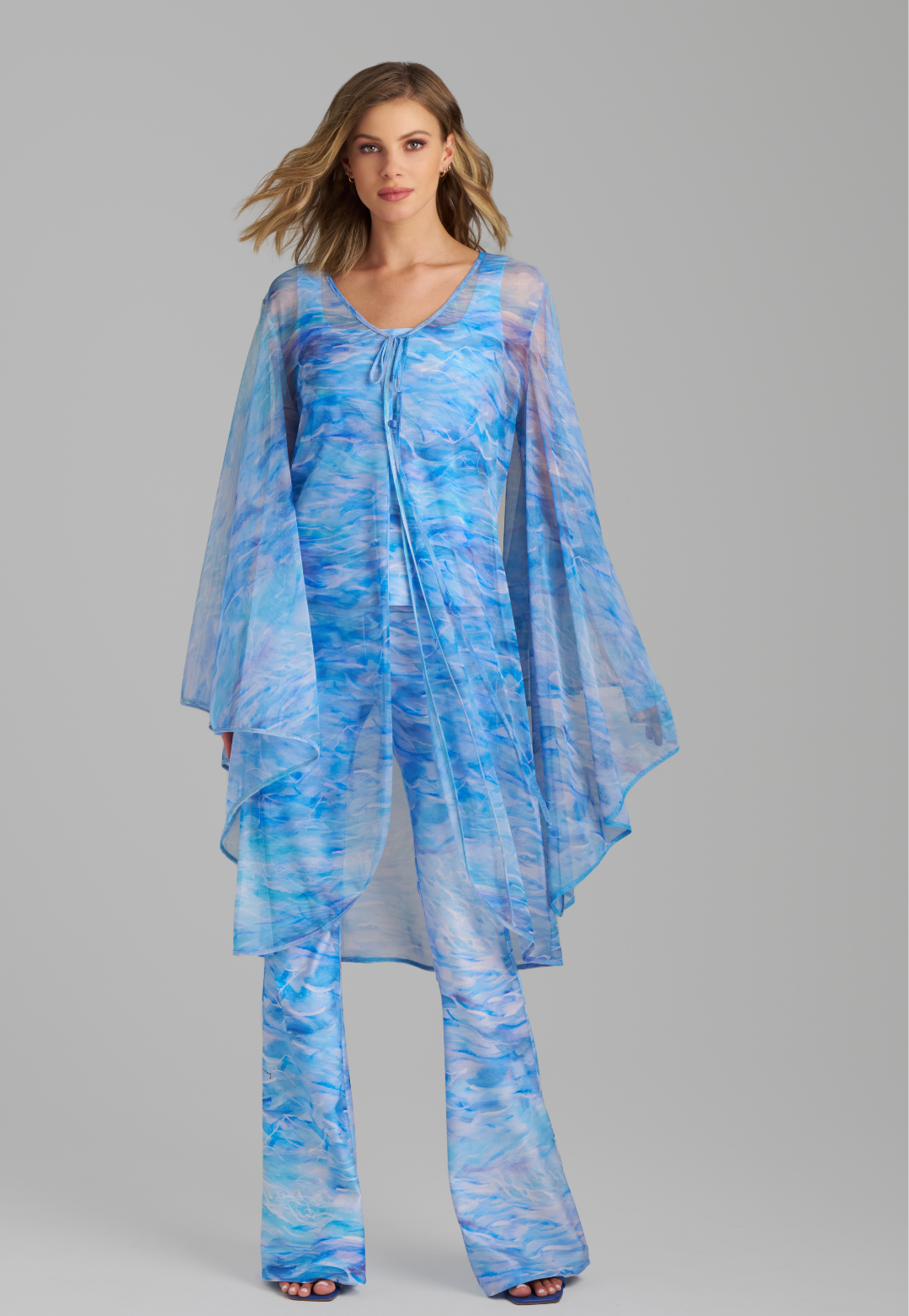 Woman wearing ocean wave printed mesh blue duster with angel sleeves over periwinkle stretch knit tank top and pants by Ala von Auersperg for summer 2023