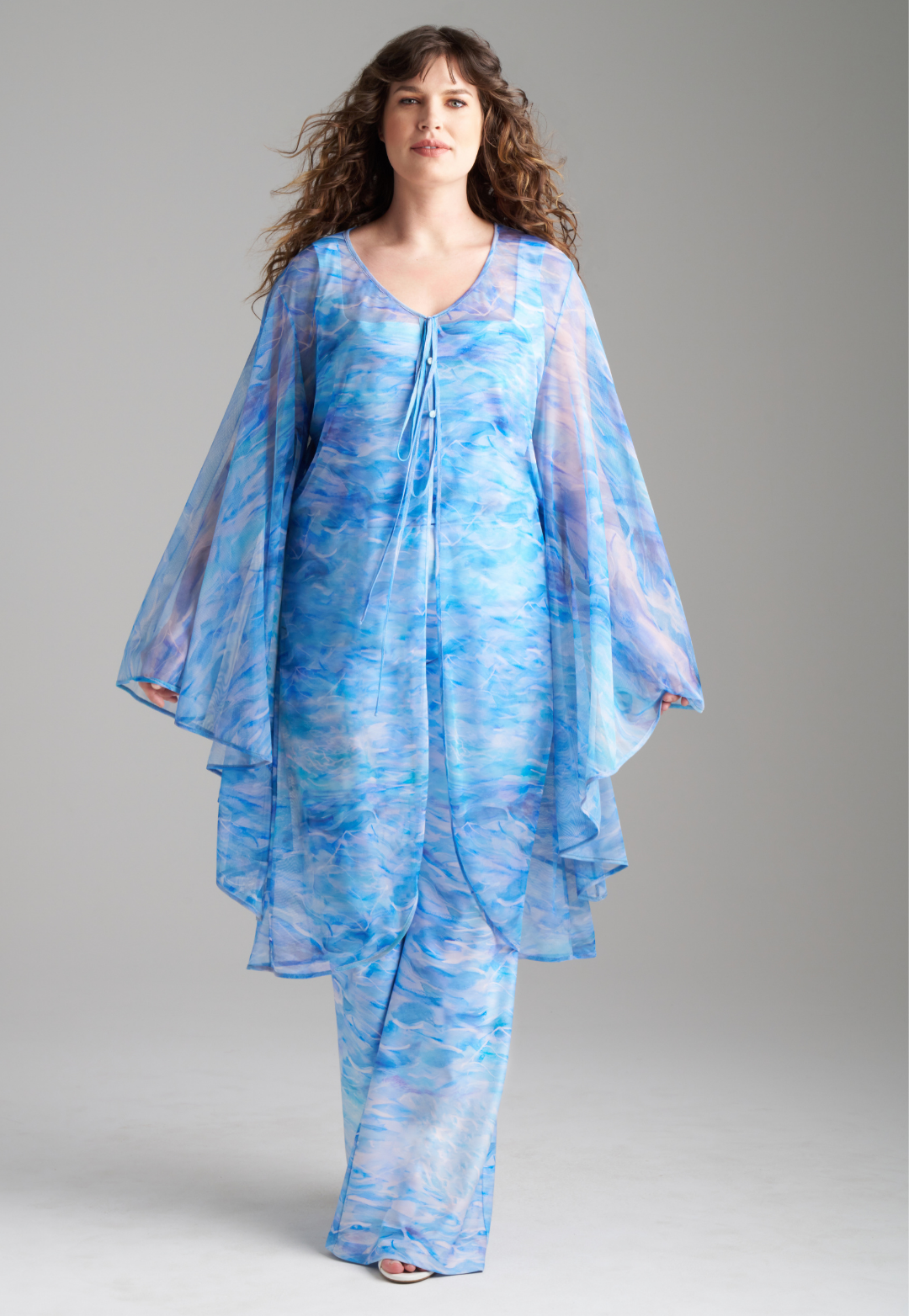 Woman wearing ocean wave printed mesh blue duster with angel sleeves over periwinkle stretch knit tank top and pants by Ala von Auersperg for summer 2023