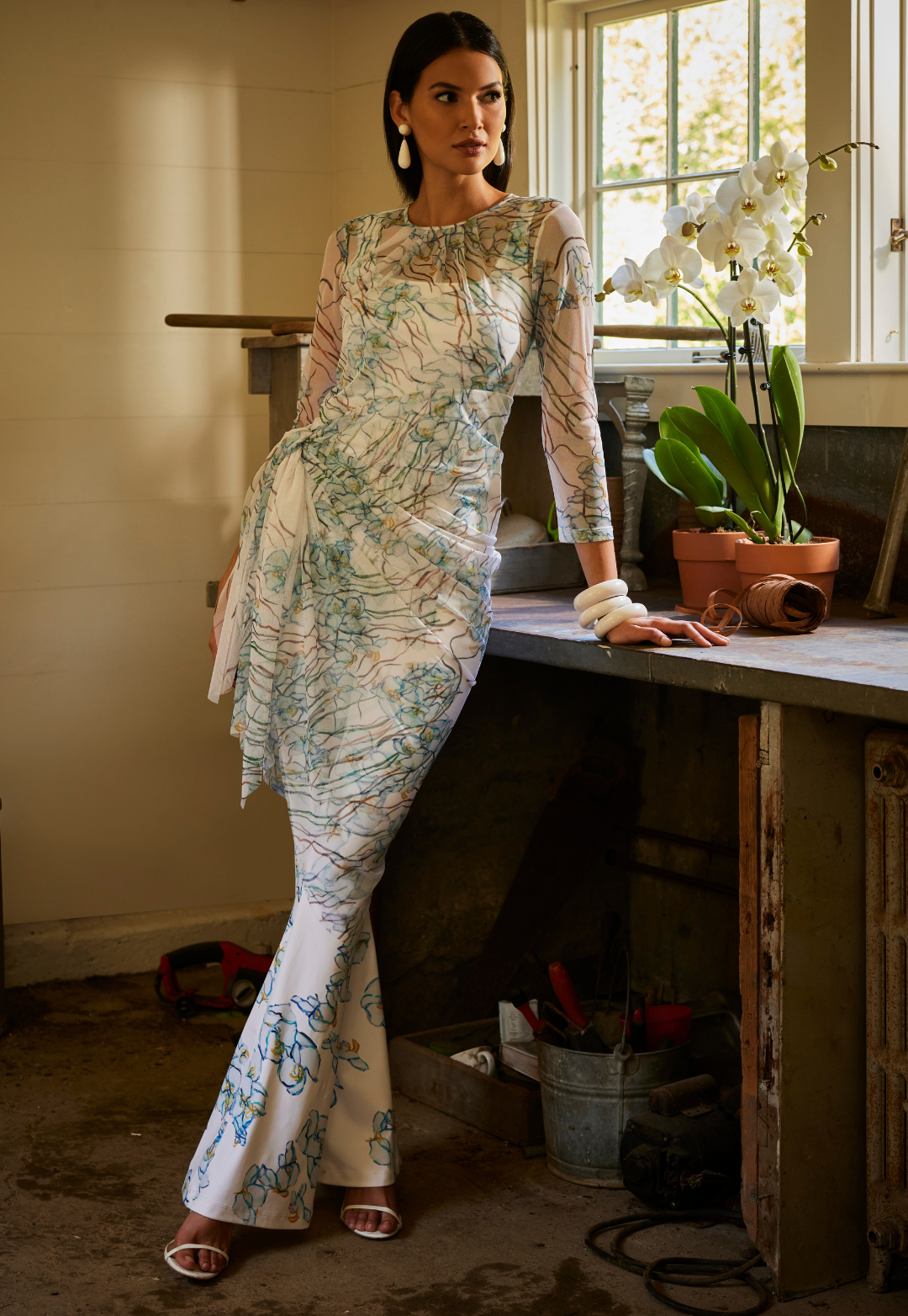 Woman in her greenhouse wearing mesh orchid printed white topper with matching stretch knit tank top and stretch pants by Ala von Auersperg for spring 2024