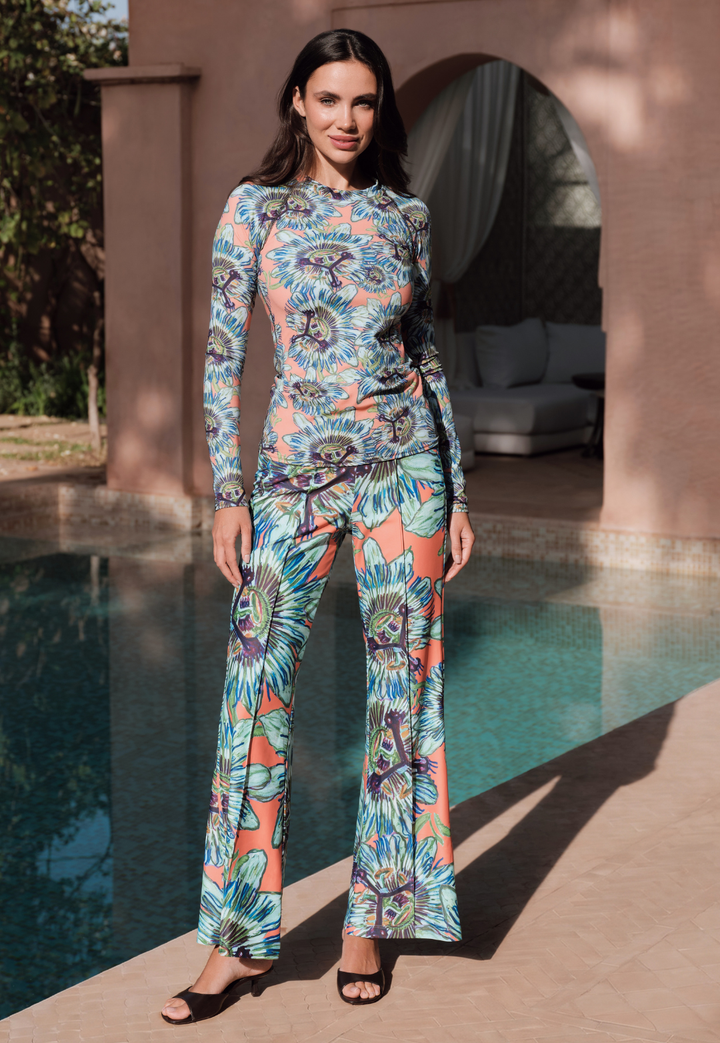 Woman in a colorful floral rashguard and pants standing by a poolside.