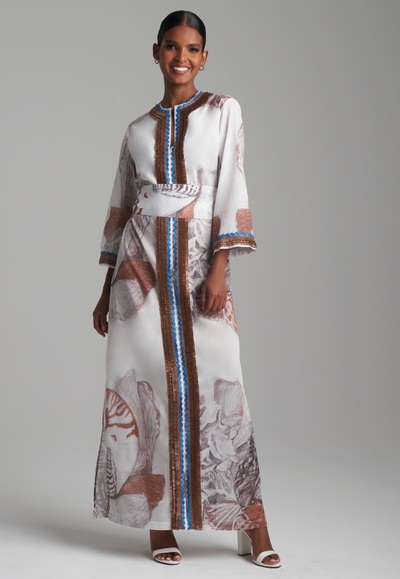 Woman wearing white shell printed cotton kaftan with brown trim and matching belt by Ala von Auersperg for resort 2024