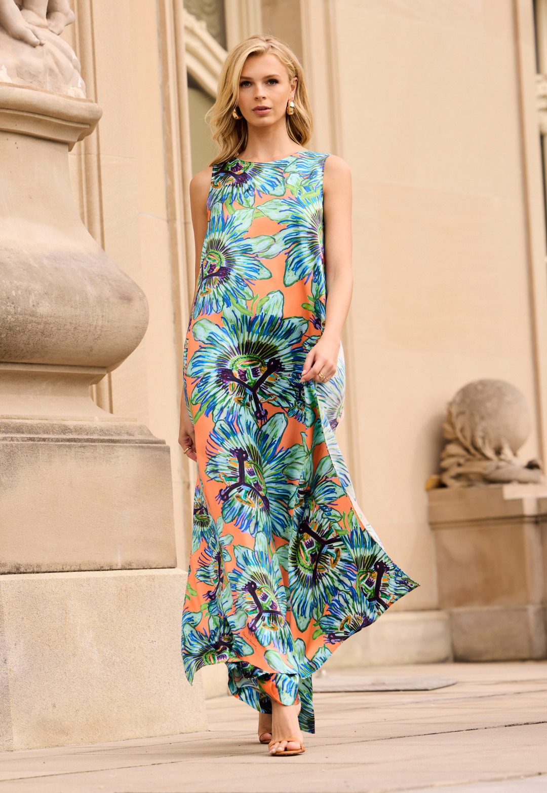 Woman wearing a colorful floral top and pants standing in front of classical architecture.