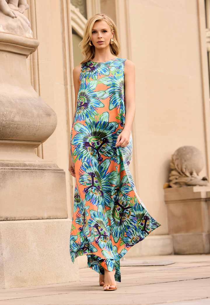 Woman wearing a colorful floral top and pants standing in front of classical architecture.