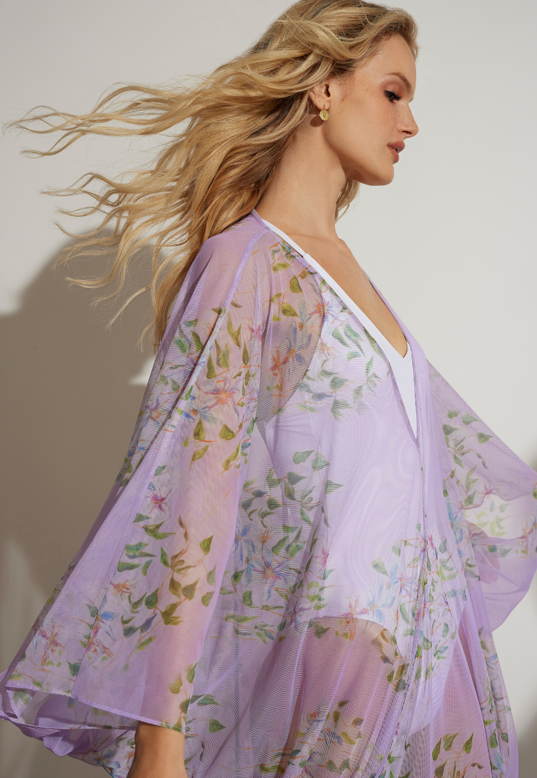 Woman wearing purple floral mesh cover up over a white bathing suit 