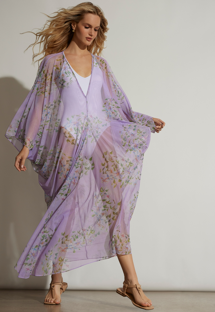 Woman wearing long mesh kaftan in a floral print with purple background over a white one piece bathing suit