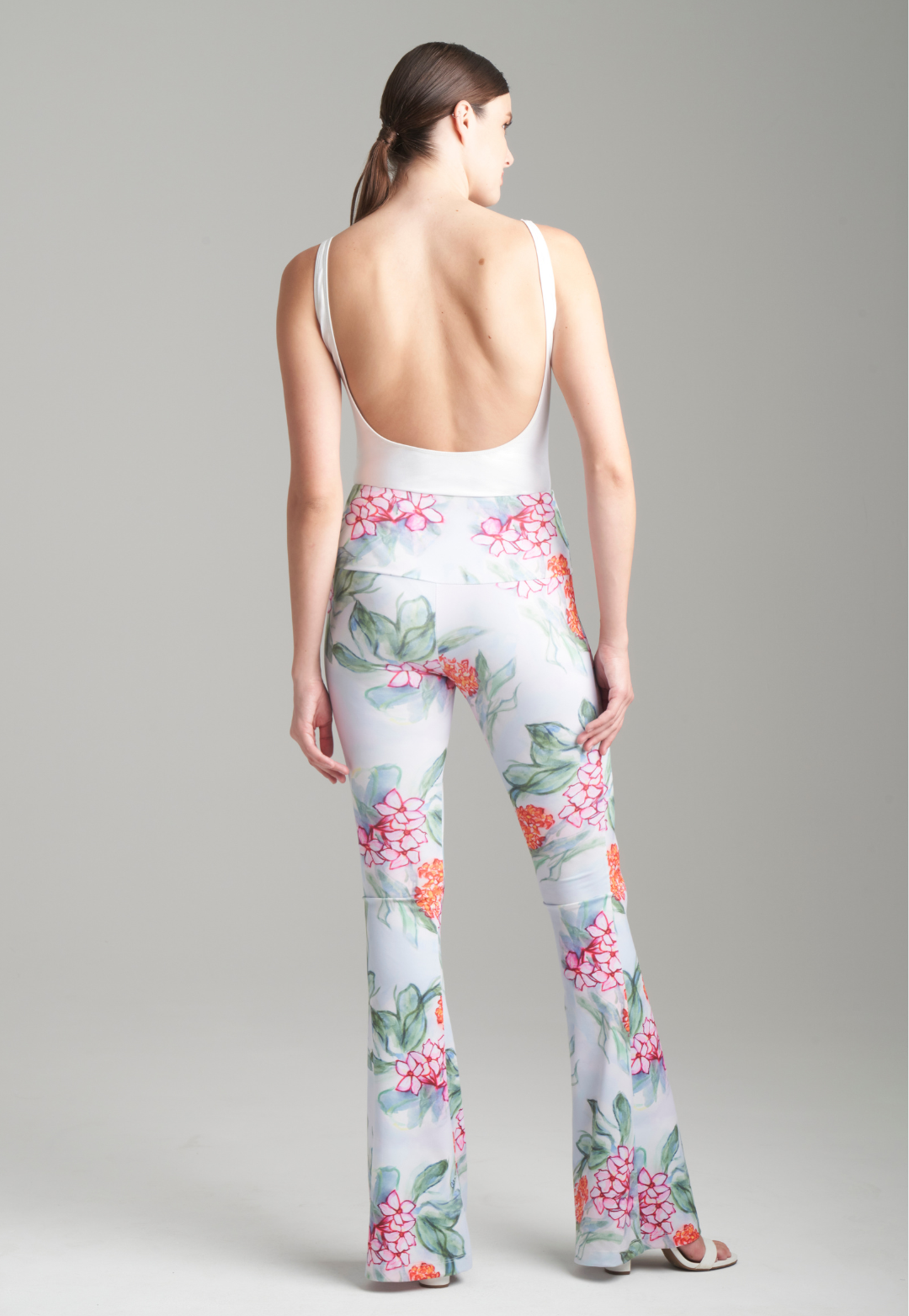 Woman wearing stretch knit floral printed pants with a flare leg and white tank top by Ala von Auersperg