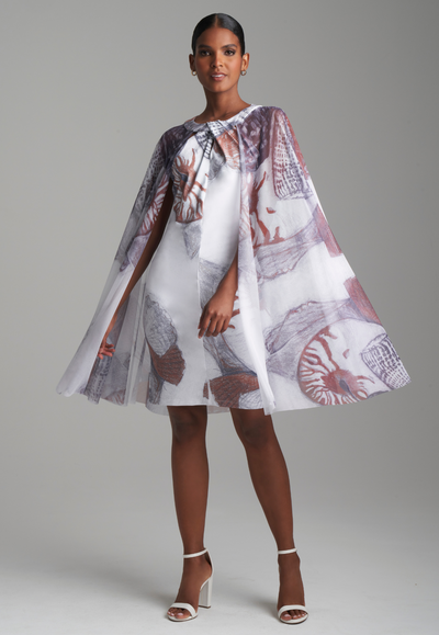 Woman wearing shell printed white stretch knit short dress with mesh capelete attached for resort 2024 by Ala von Auersperg