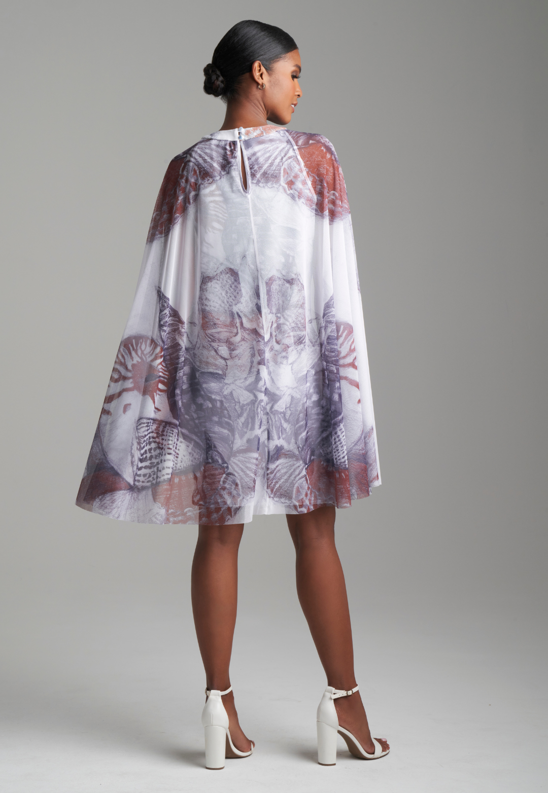 Woman wearing shell printed white stretch knit short dress with mesh capelet attached for resort 2024 by Ala von Auersperg