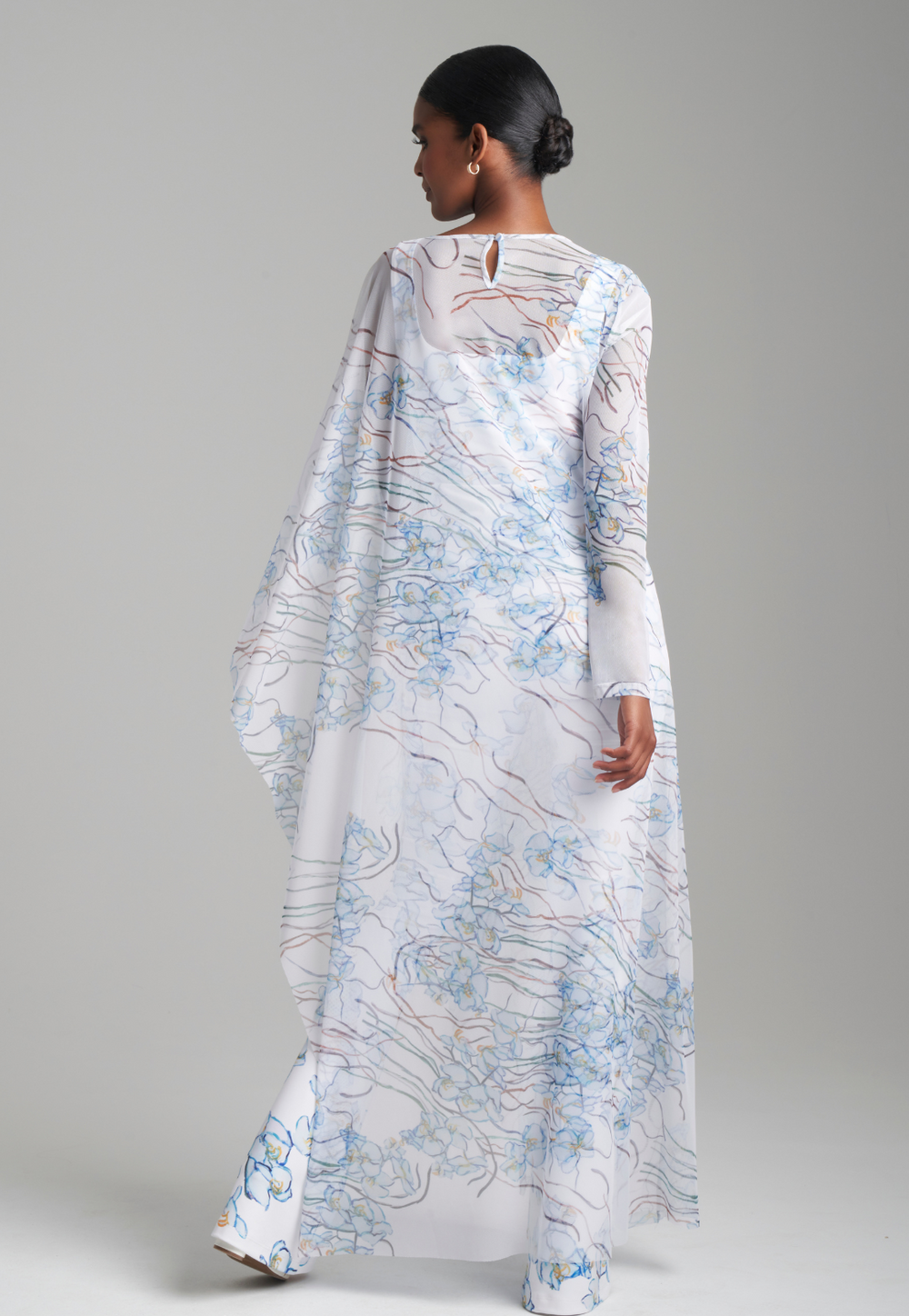 Woman wearing white and blue mesh one armed kaftan poncho over matching tank top and pants by Ala von Auersperg for spring 2024