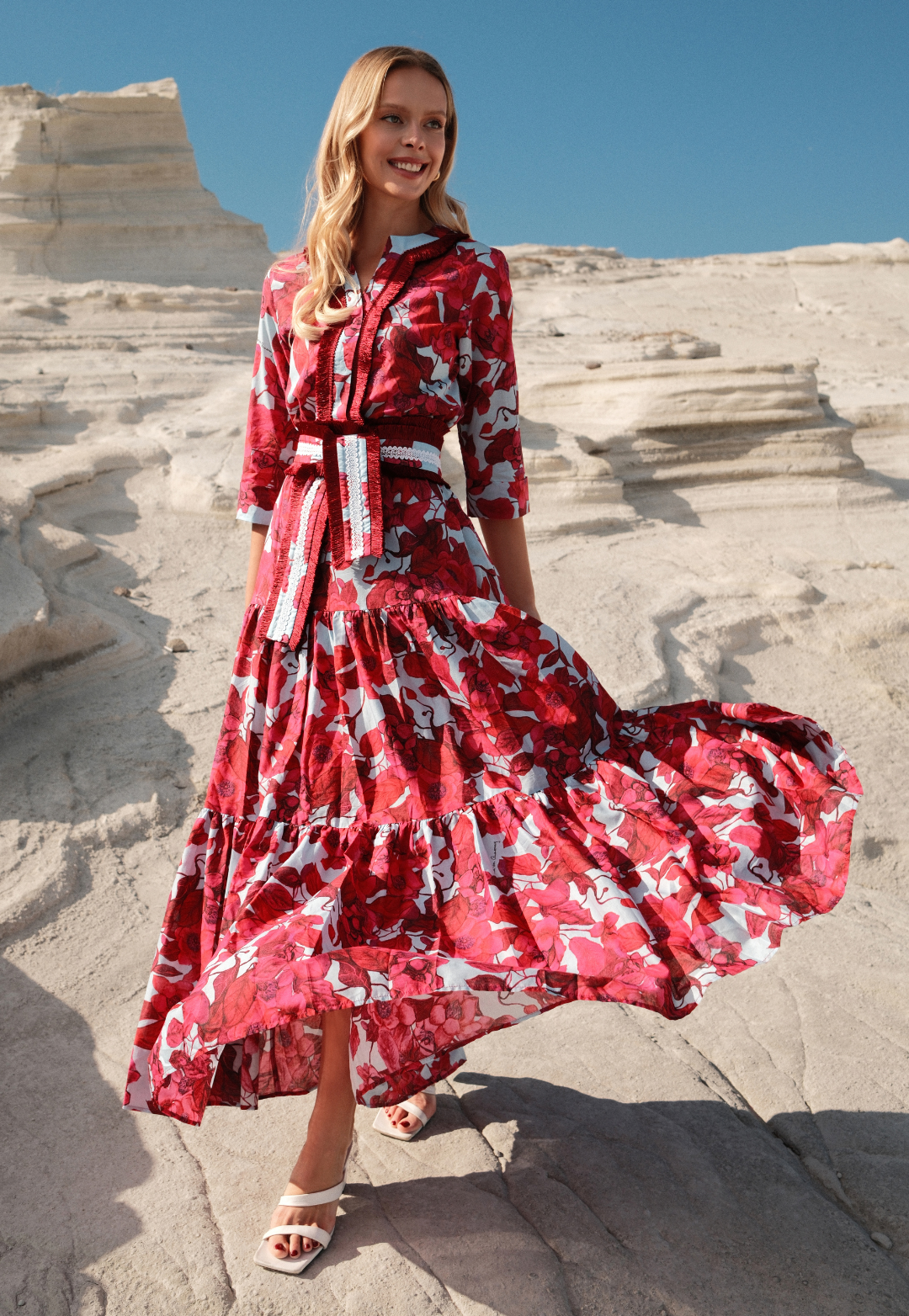 Woman in a red floral dress standing on a stone staircase with a clear blue sky.