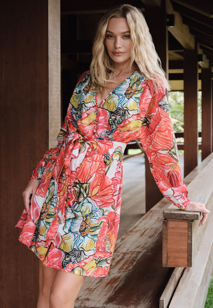 Woman wearing a colorful floral dress standing on a wooden deck.