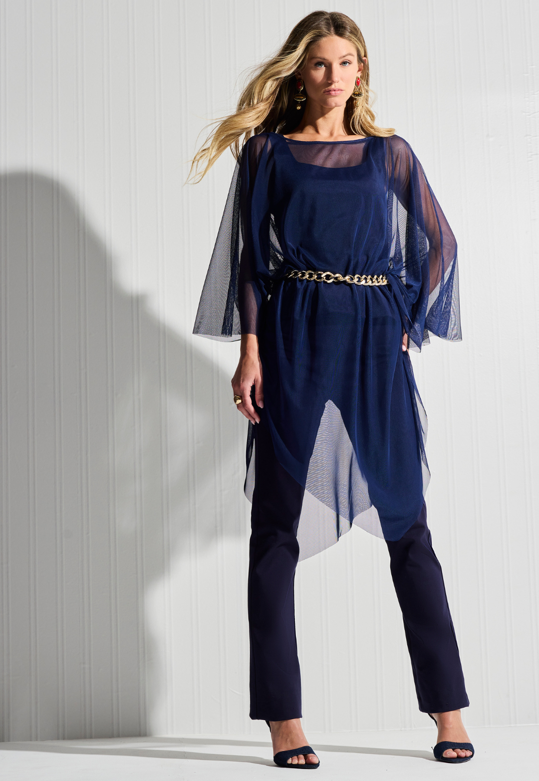 Woman wearing sheer mesh navy poncho over navy tank top and pants with a gold chain belt by designer Ala von Auersperg for womens luxury travel clothing