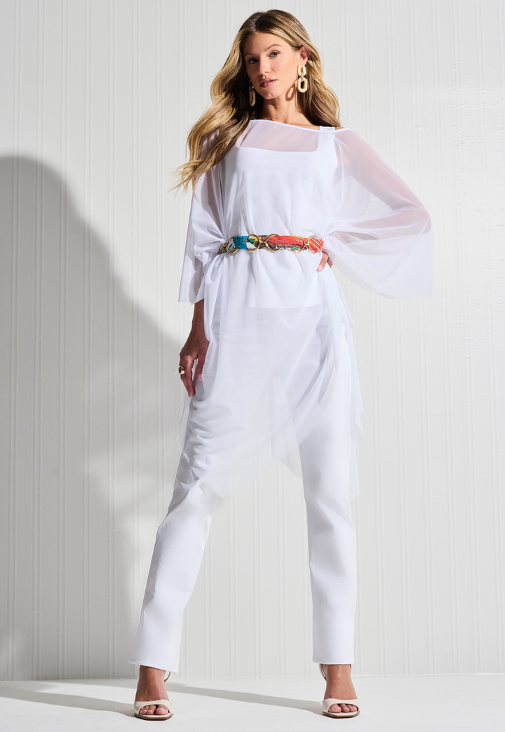 Woman wearing white mesh poncho over white tank top and pants with a belt by designer Ala von Auersperg for womens luxury travel clothing
