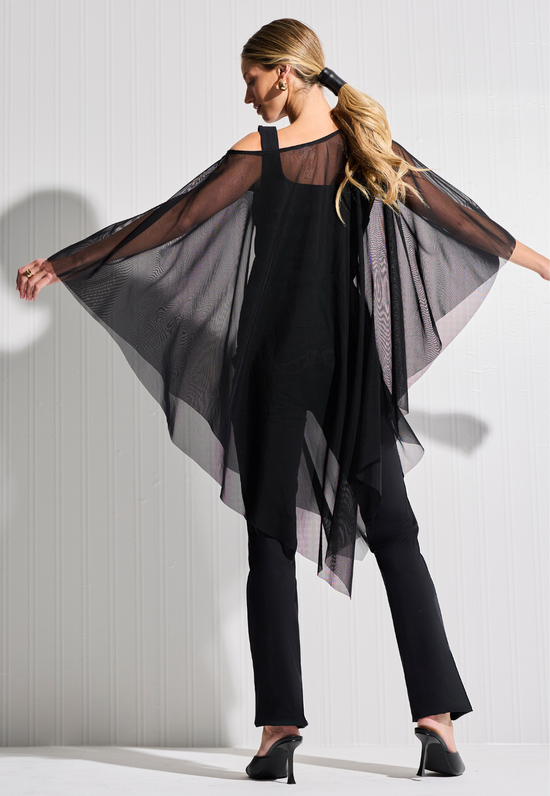 Woman wearing long sheer black mesh poncho over matching tank top and pants in black by designer Ala von Auersperg for womens luxury travel clothing