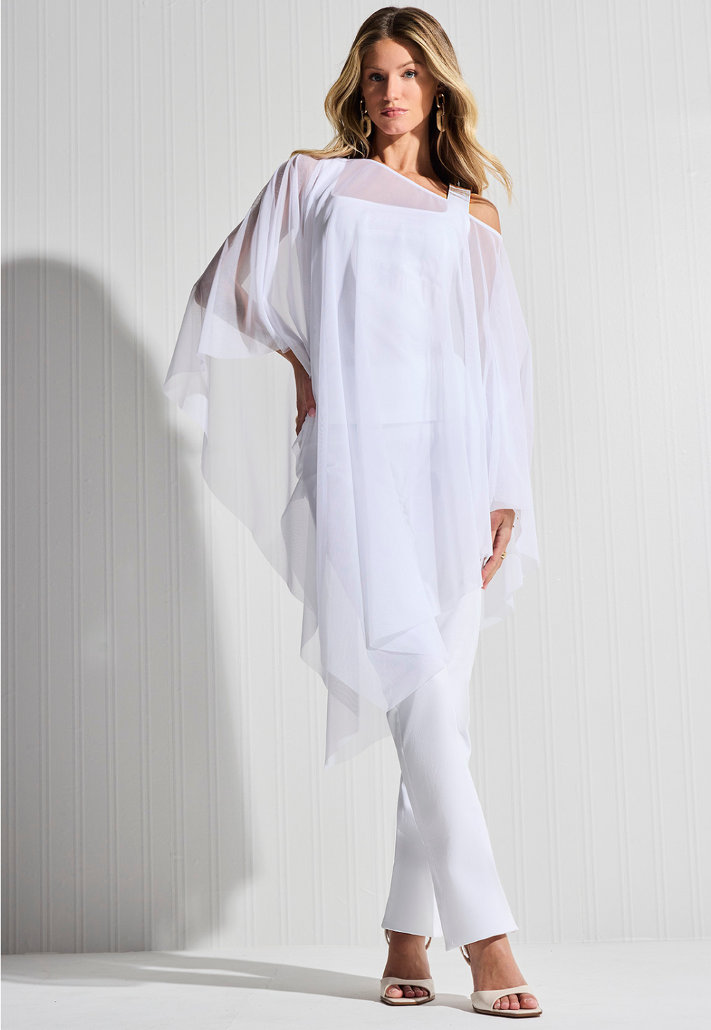 Woman wearing white mesh poncho over white cotton tank top and white cotton pants by designer Ala von Auersperg for womens luxury travel clothing