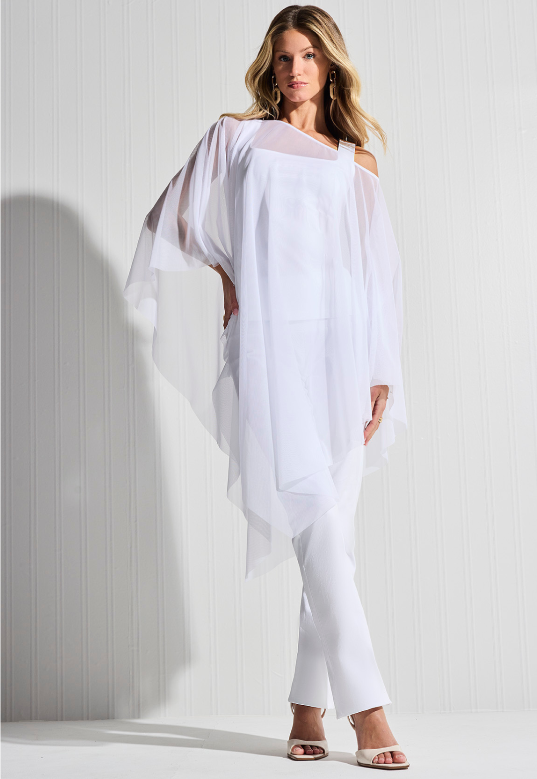 Woman wearing white mesh poncho over white cotton tank top and white cotton pants by designer Ala von Auersperg for womens luxury travel clothing