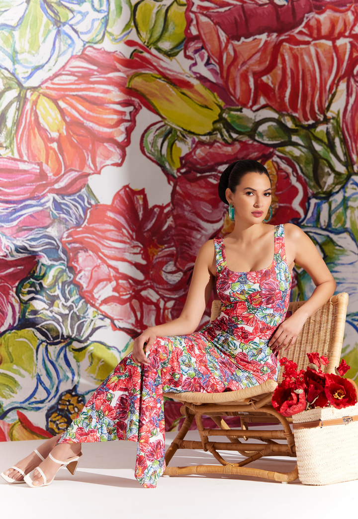 Woman sitting in a chair wearing a long stretch knit dress in a red floral print by designer Ala von Auersperg for womens luxury travel clothing