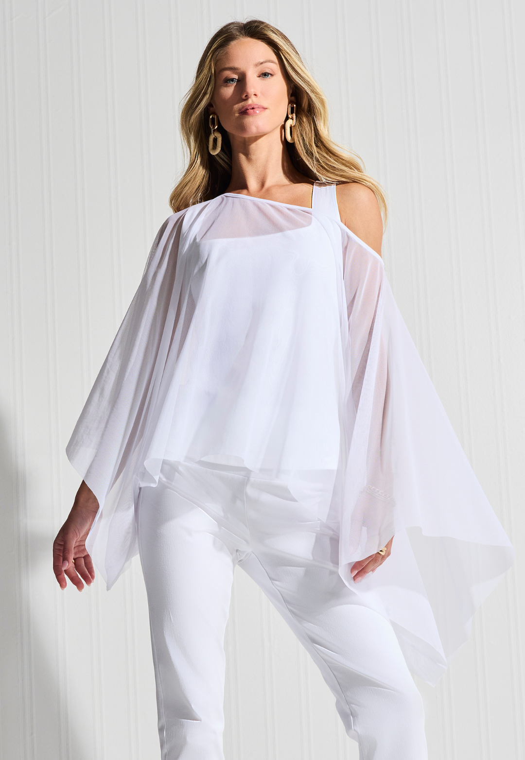 Woman wearing short white mesh top over white tank top and pants by designer Ala von Auersperg for womens luxury travel clothing