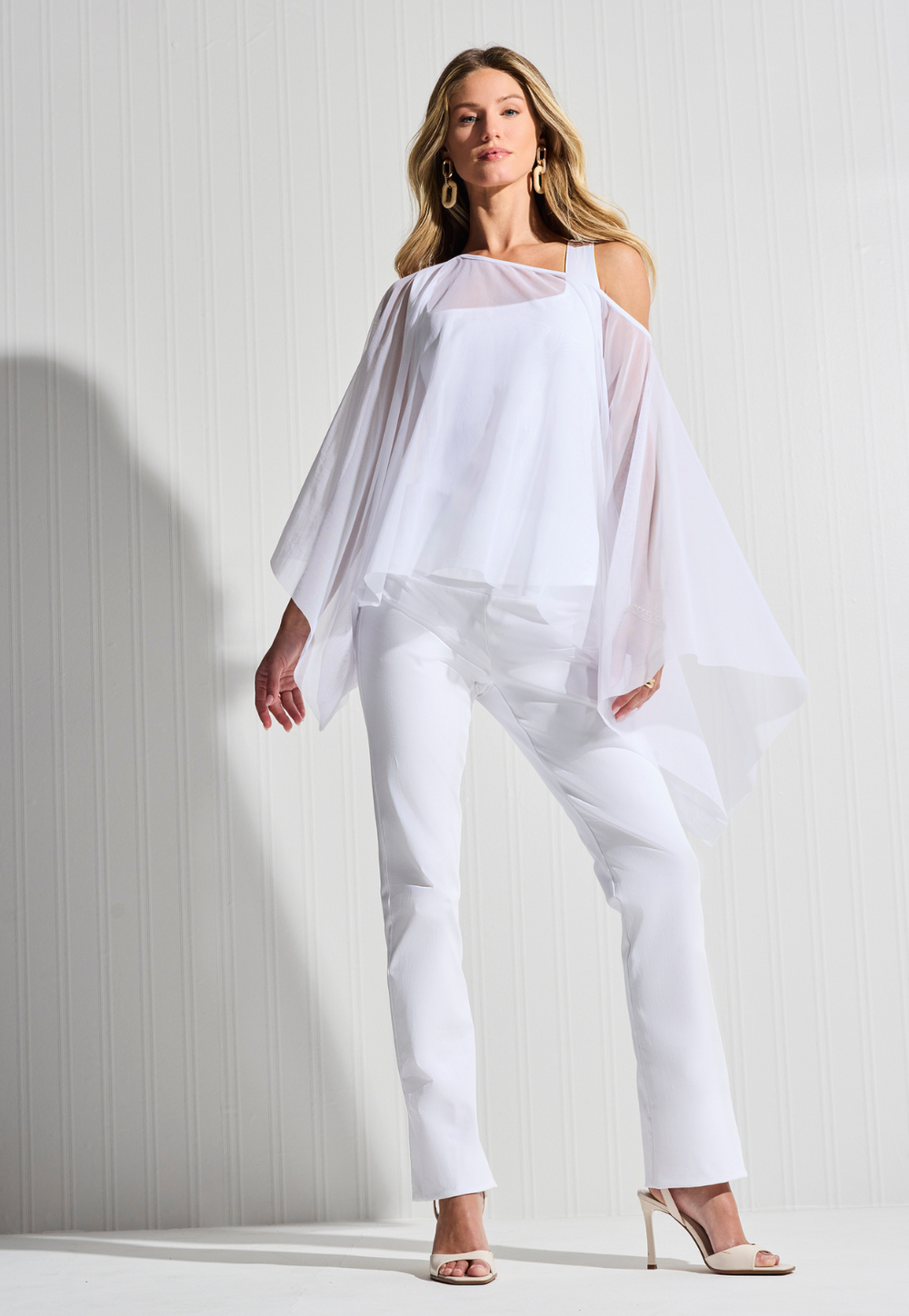 Woman wearing white sheer poncho over white tank top and white pants by designer Ala von Auersperg for womens luxury travel clothing