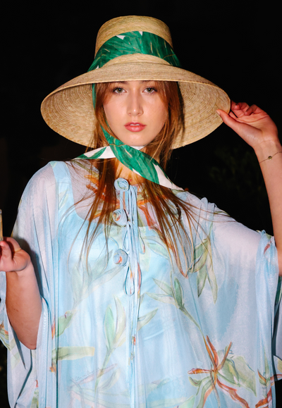 Woman wearing Sarah Bray Bermuda straw hat with Ala von Auersperg palm leaf printed cotton ribbon with mesh kaftan dress topper over long stretch knit dress