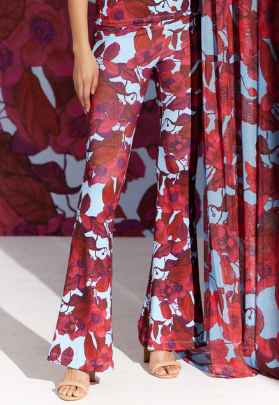 Woman wearing stretch knit red floral pants with a blue background by designer Ala von Auersperg for womens luxury travel clothing