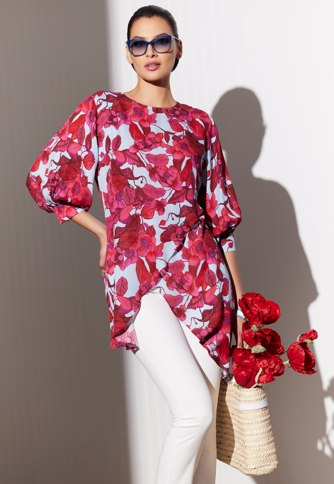 Woman wearing silk blouse in a red floral print with white italian stretch cotton pants and a straw bag by designer Ala von Auersperg for womens luxury travel clothing