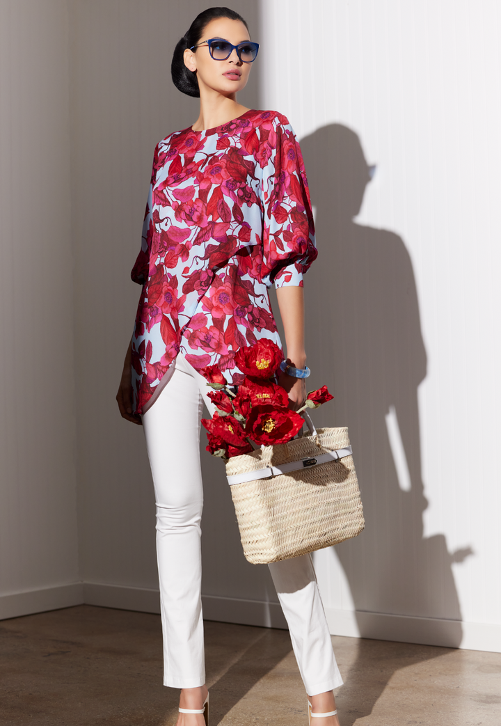 Woman wearing silk printed blouse in a red floral print with italian stretch cotton pants and a straw bag by designer Ala von Auersperg for womens luxury travel clothing