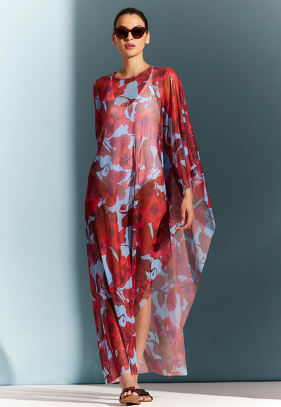 Woman wearing sheer mesh poncho cover up over a bathing suit in a red floral print with a blue background by designer Ala von Auersperg for womens luxury travel clothing