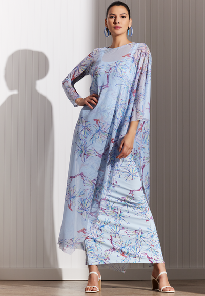 Woman wearing blue floral printed sheer kaftan over a long stretch knit dress in the matching print by designer Ala von Auersperg for womens luxury travel clothing