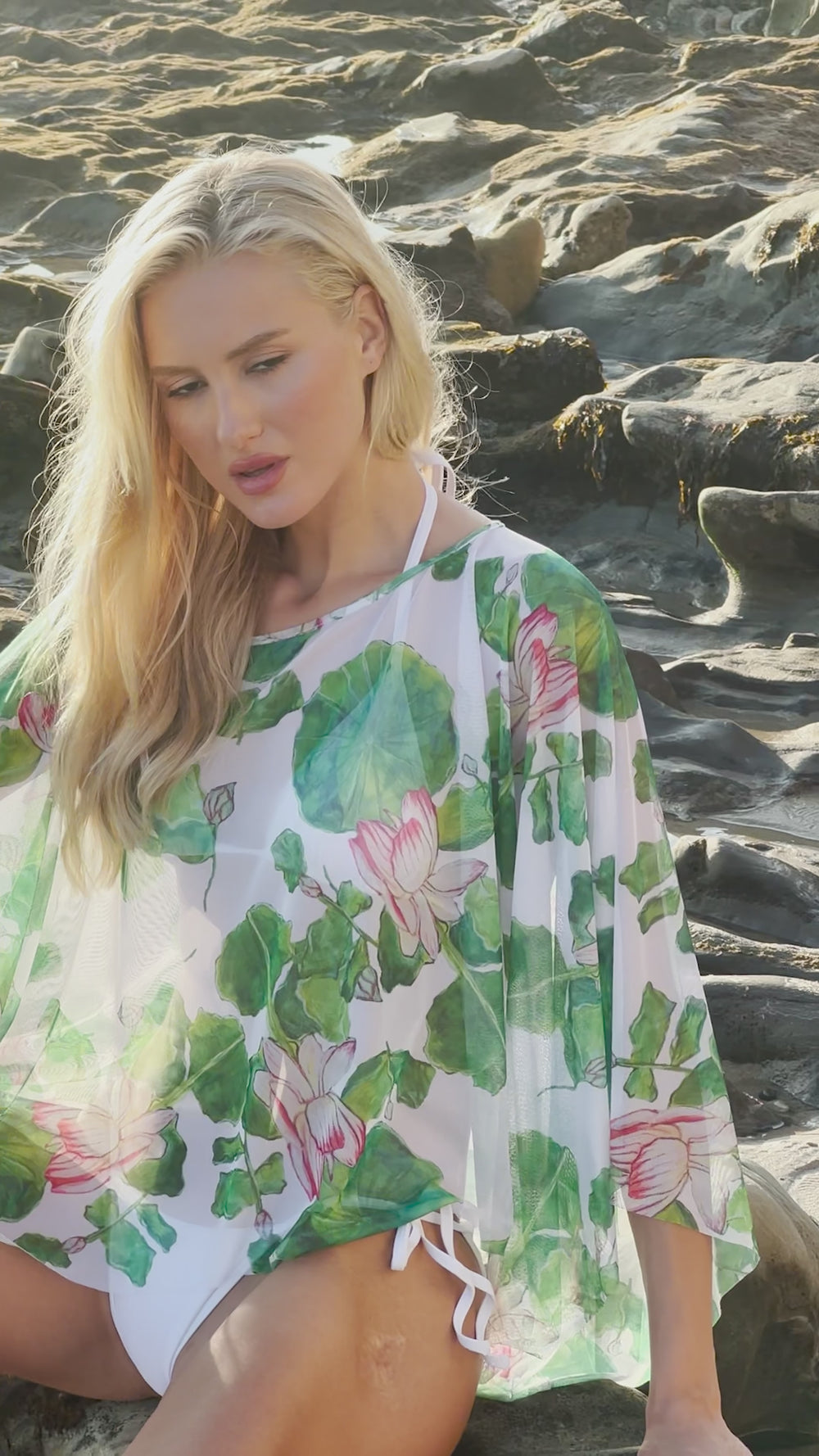 Video of a woman wearing a mesh floral poncho over a bathing suit on the beach