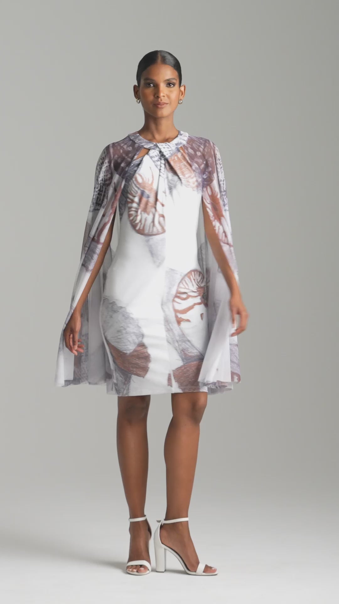 Woman wearing shell printed white stretch knit short dress with mesh capelet attached for resort 2024 by Ala von Auersperg