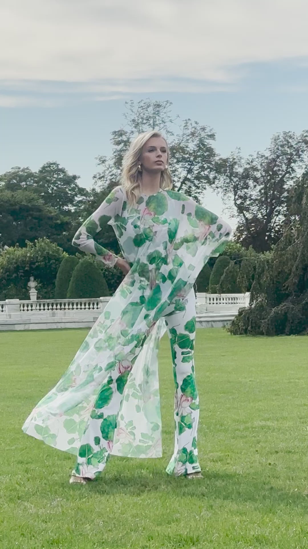 Video of a woman wearing a mesh poncho over a tank top and pants in a matching lillypad and floral print