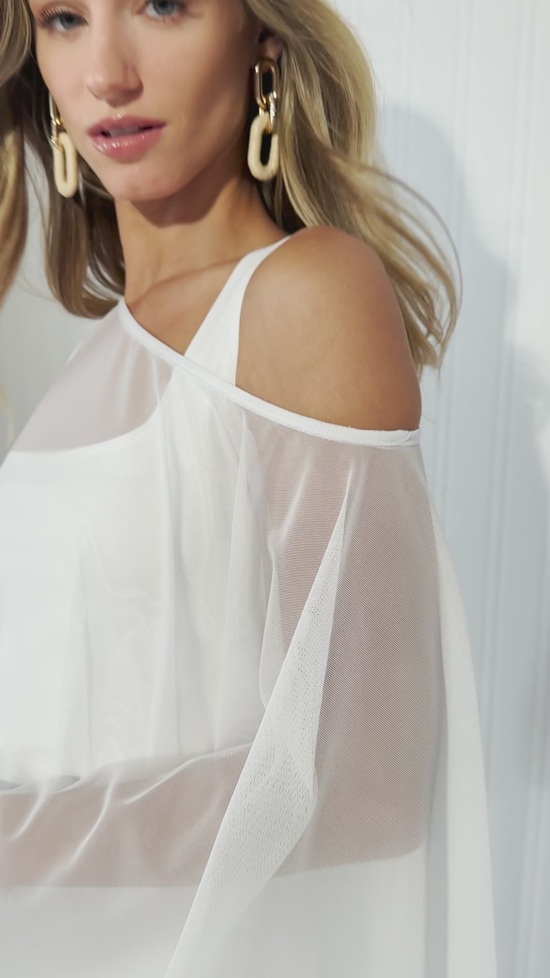 Video of a woman wearing a white sheer mesh cover up over white cotton tank top and white cotton pants by designer Ala von Auersperg for womens luxury travel clothing